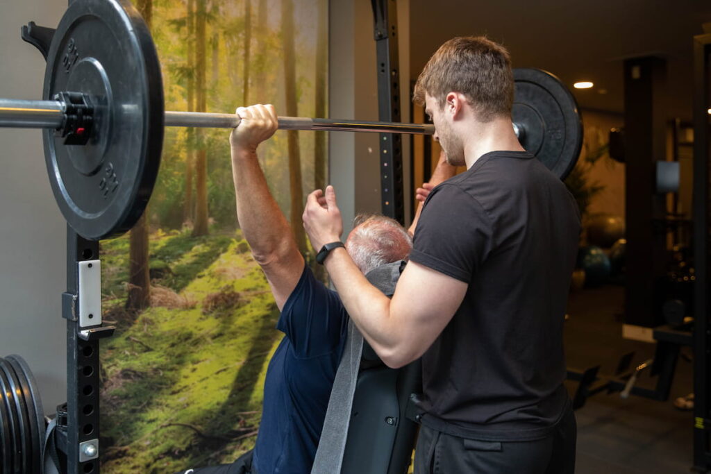 Personal trainer met cliënt die een bench press doet tijdens eentraining in de zaal